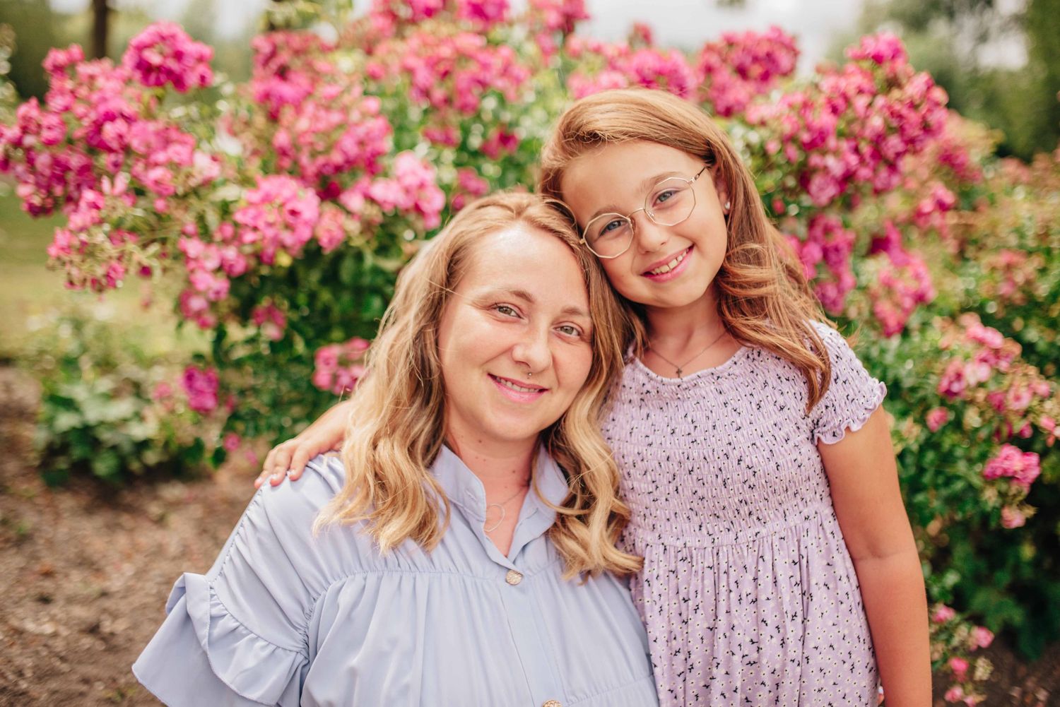 Outdoor family photoshoot among blooming pink flowers in a garden setting.