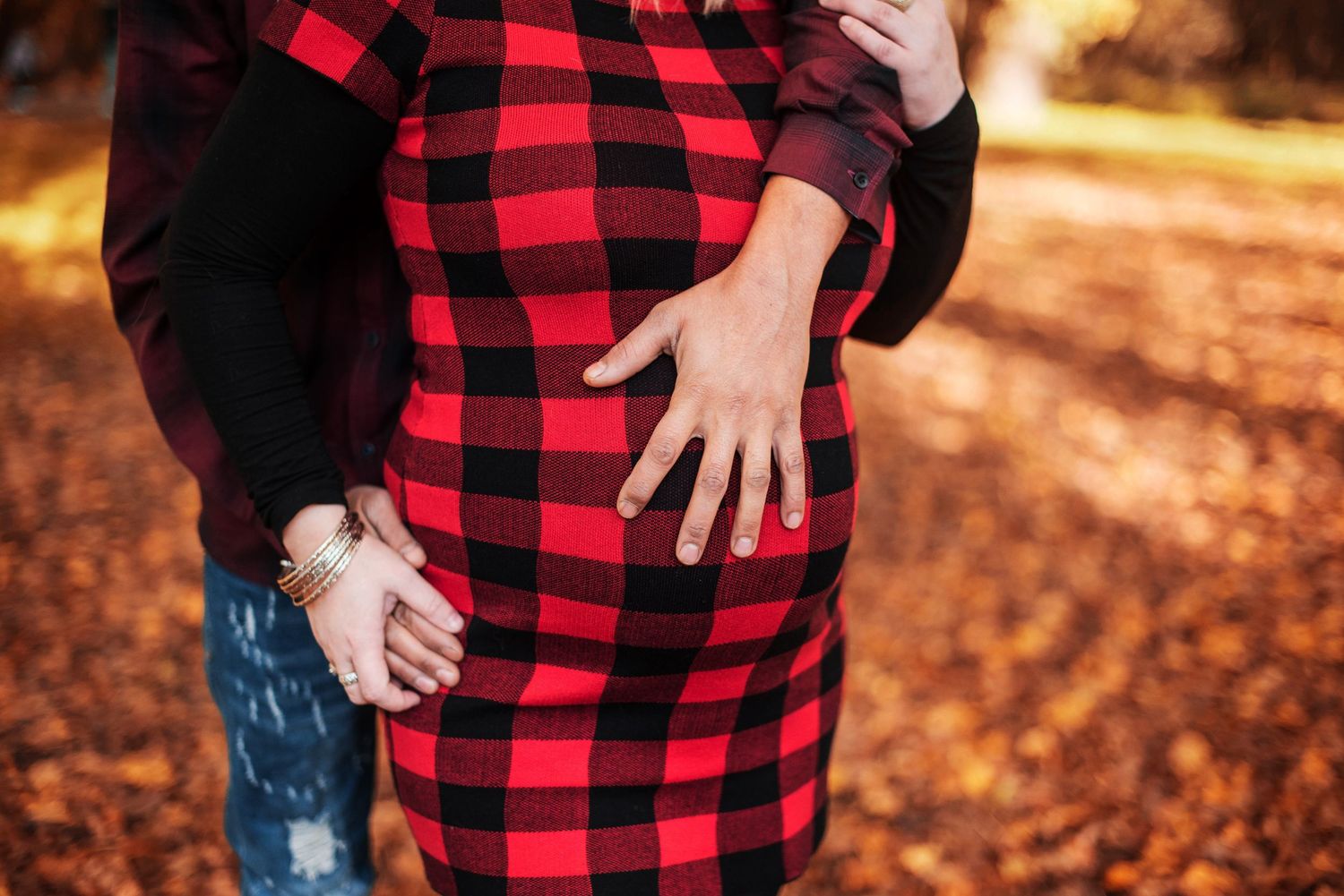 Close-up of a baby bump with hands resting on it, wearing a red and black buffalo plaid dress.