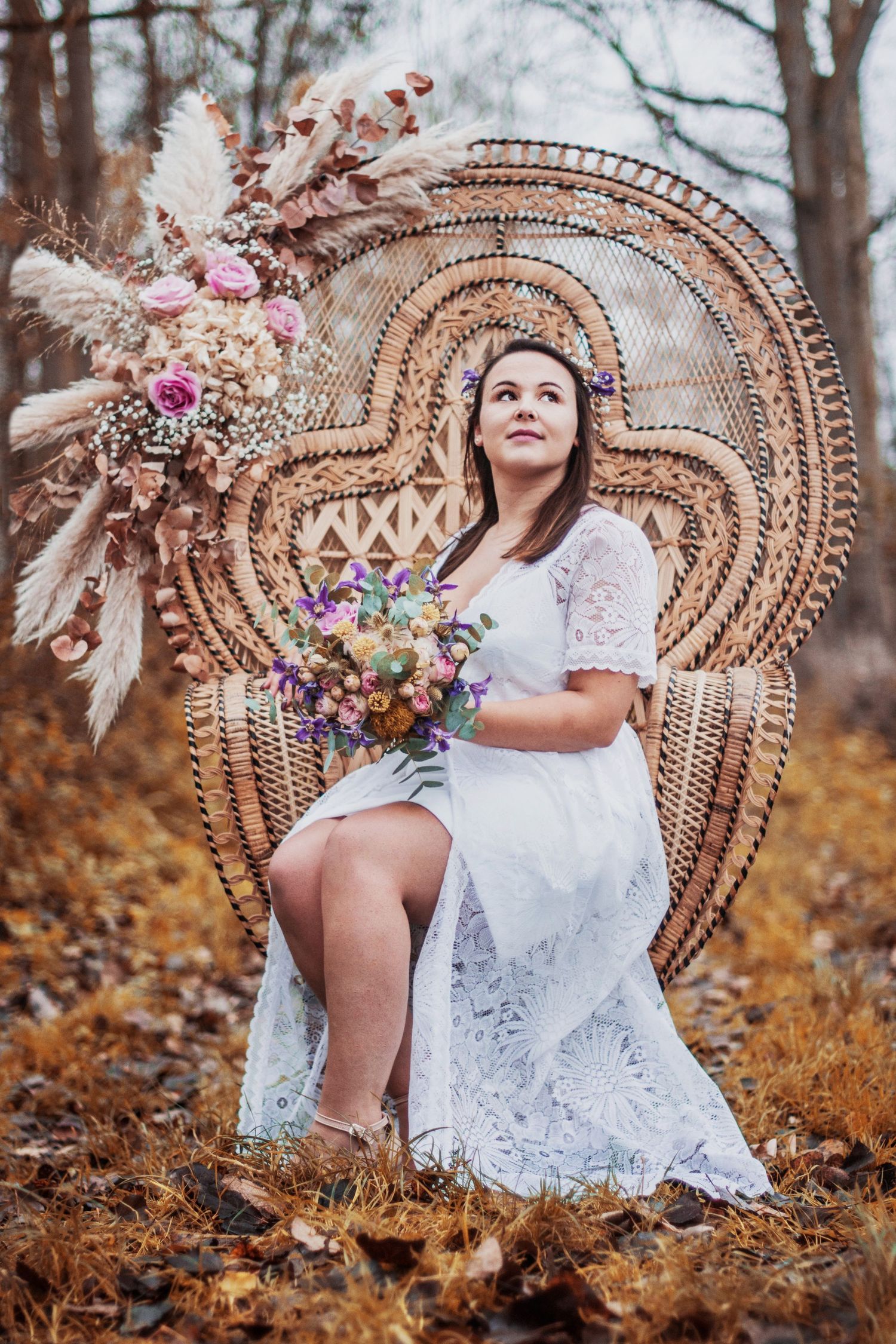 A white lace dress contrasts with an ornate wicker peacock chair in a fall setting.