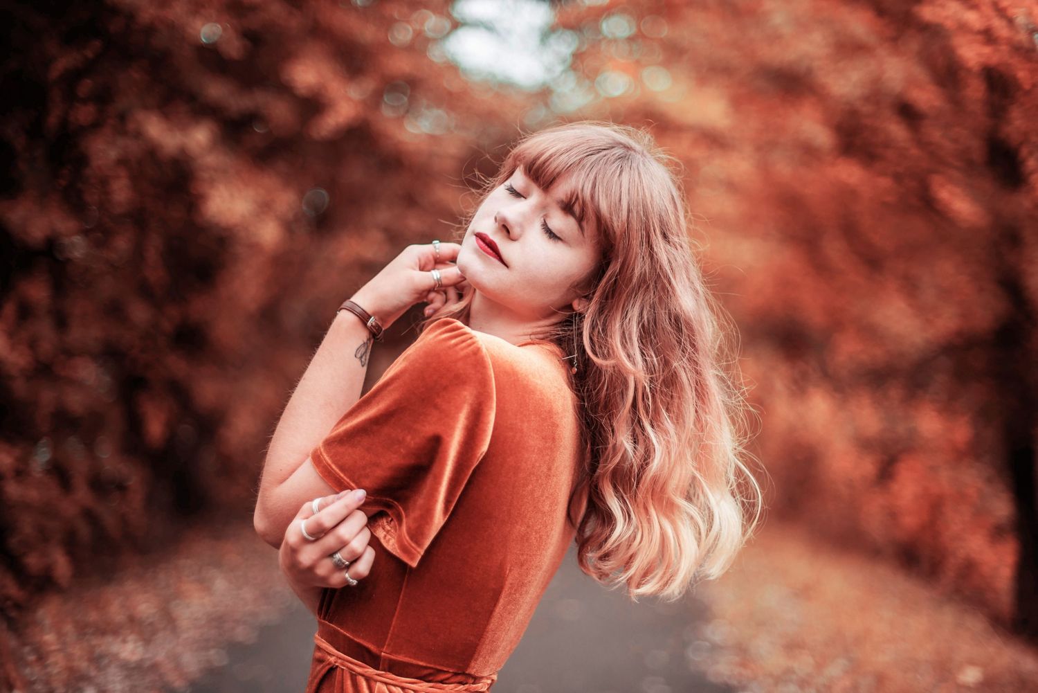 Artistic autumn portrait in orange tones showing dreamy pose against blurred foliage background.