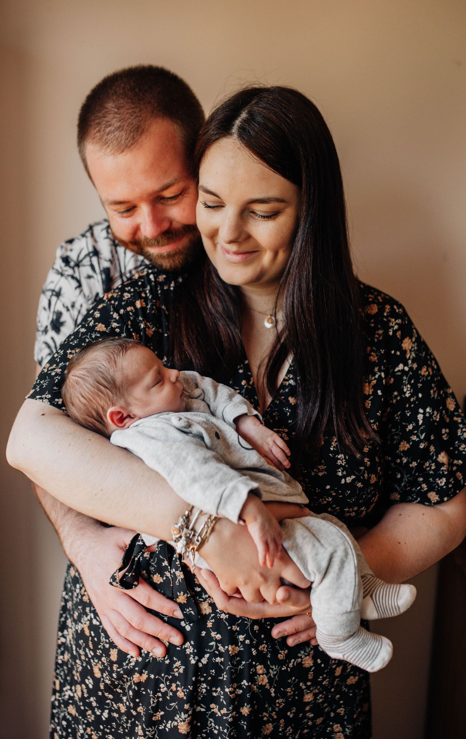 Intimate family portrait series with newborn baby against warm brown background.