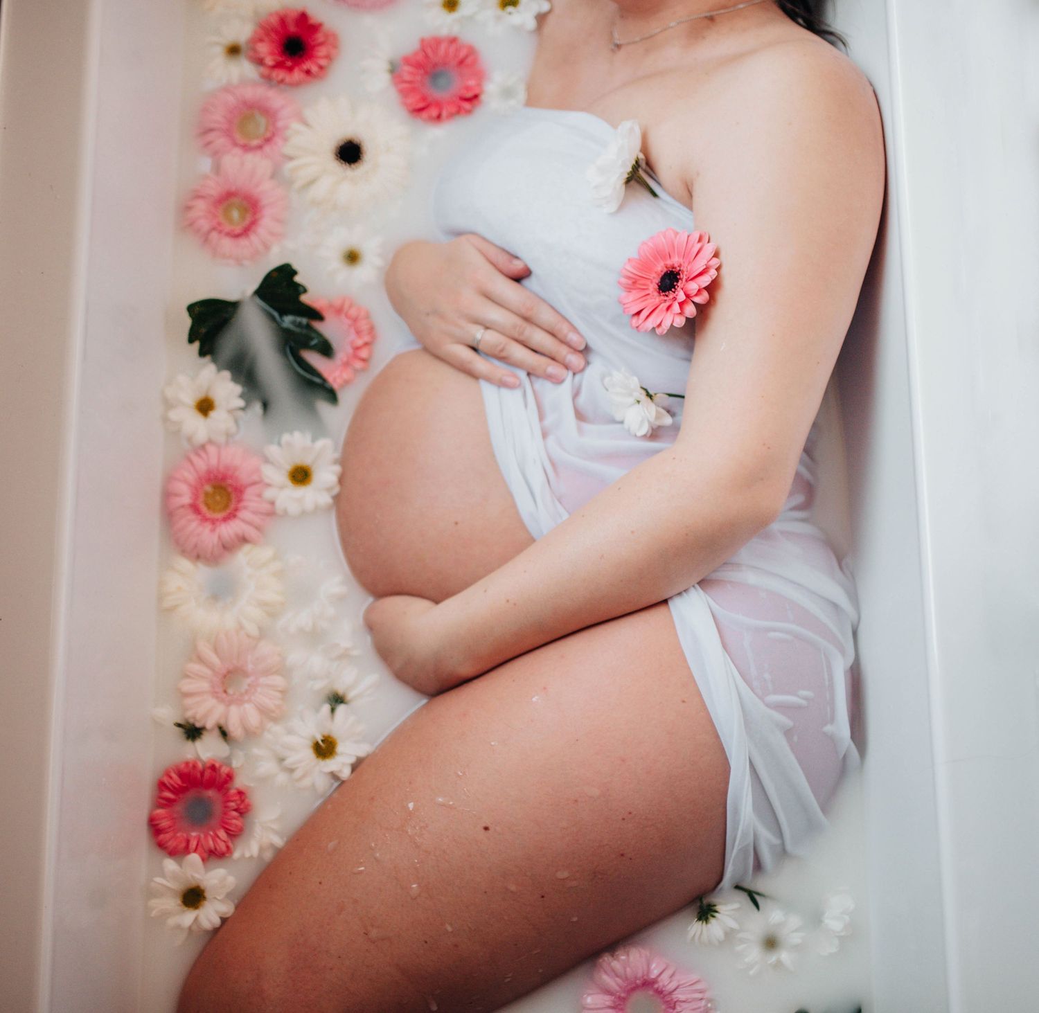 Artistic maternity bath photography with floral decorations and soft lighting.