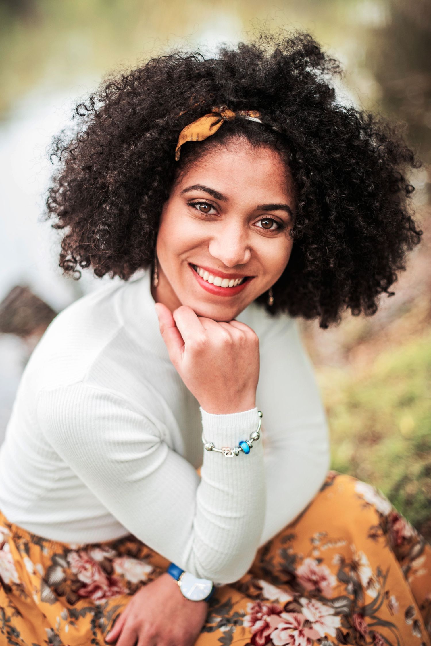 Portrait of person with natural curly hair wearing white sweater and orange headband.