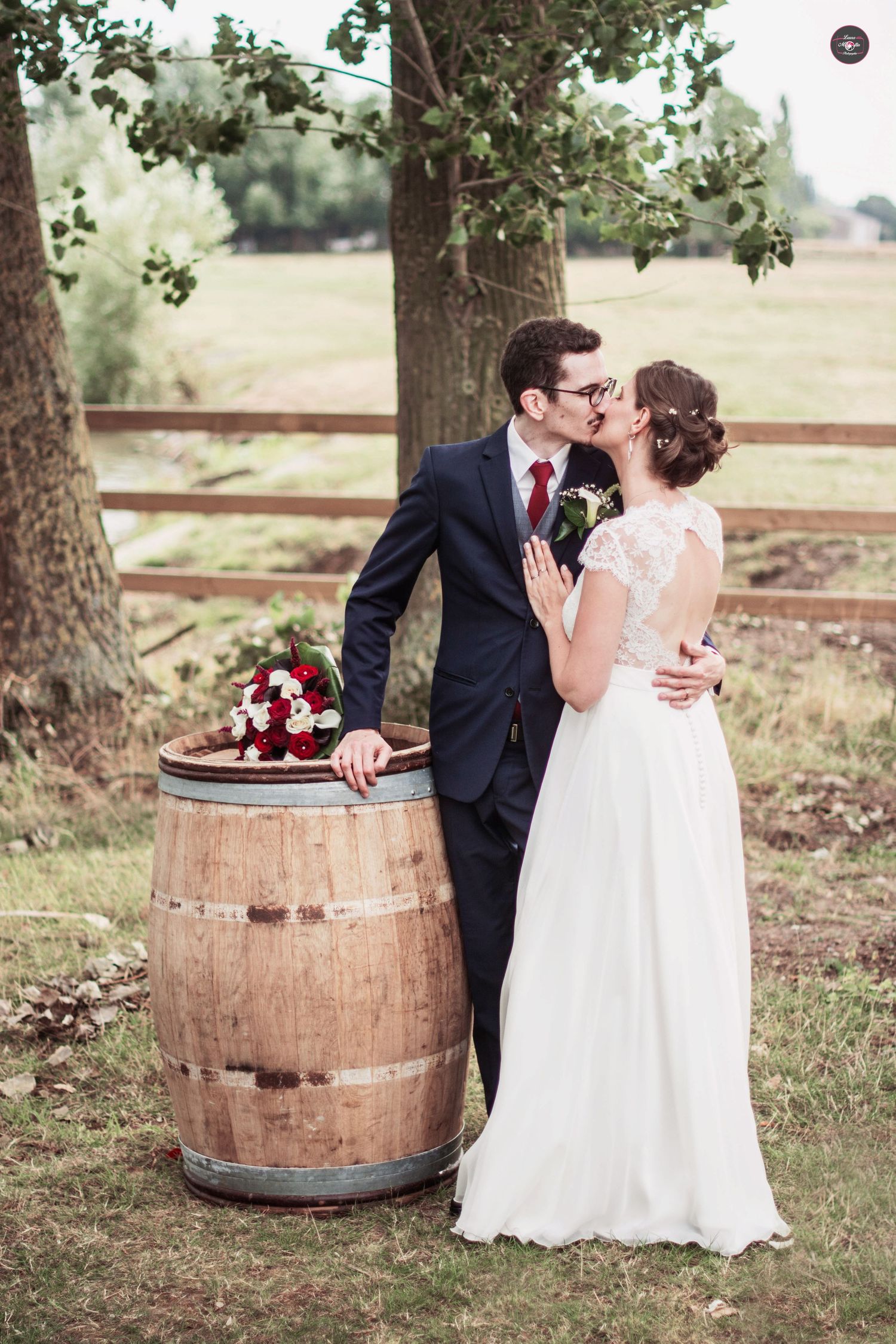 Couple posing near rustic wooden barrels in an outdoor garden setting.