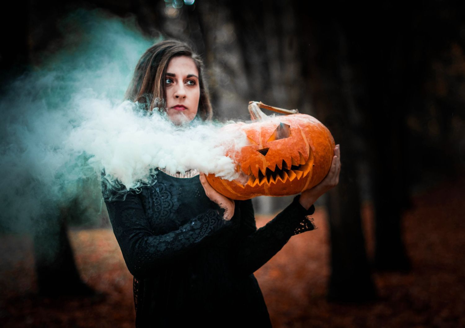 Halloween themed photo with smoking jack o'lantern in spooky forest atmosphere.