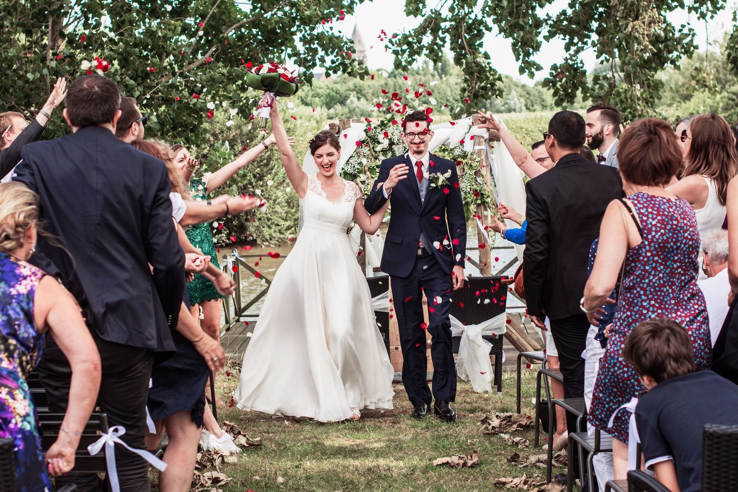 Wedding guests throw flower petals at the happy couple during an outdoor ceremony.