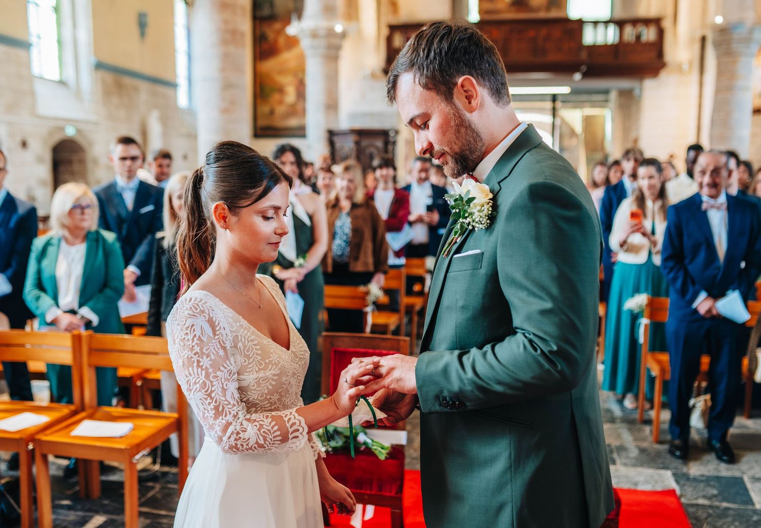 Groom placing wedding ring on bride's finger during church ceremony with guests seated in pews.