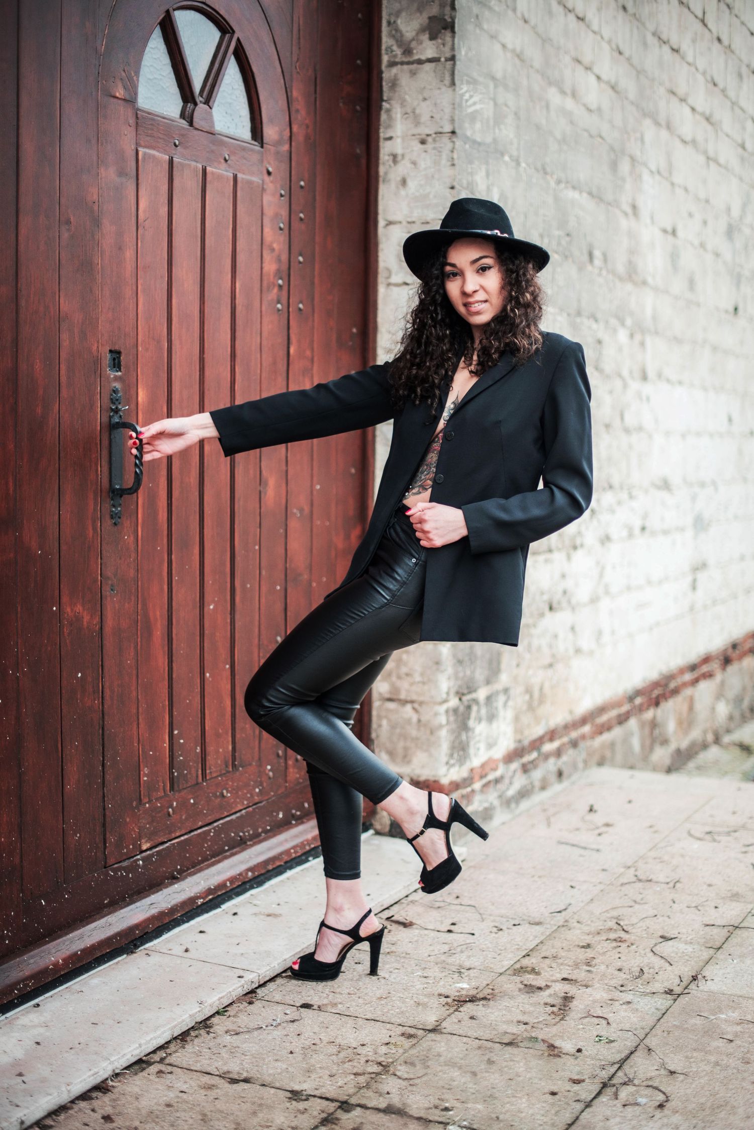 Fashion portraits featuring a model in all black attire and heels posing against a rustic wooden door.