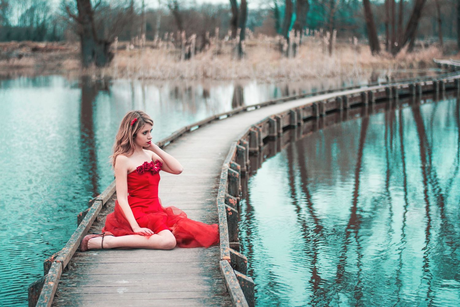 Elegant red dress flowing on a wooden boardwalk over turquoise water.