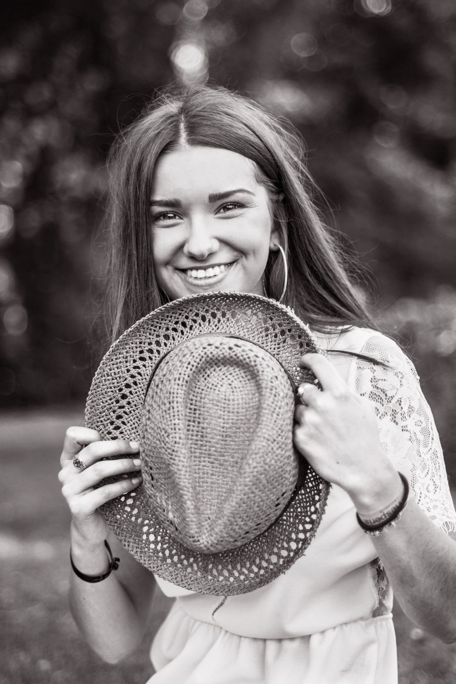 Black and white portrait showing joyful expression while holding a woven straw hat.