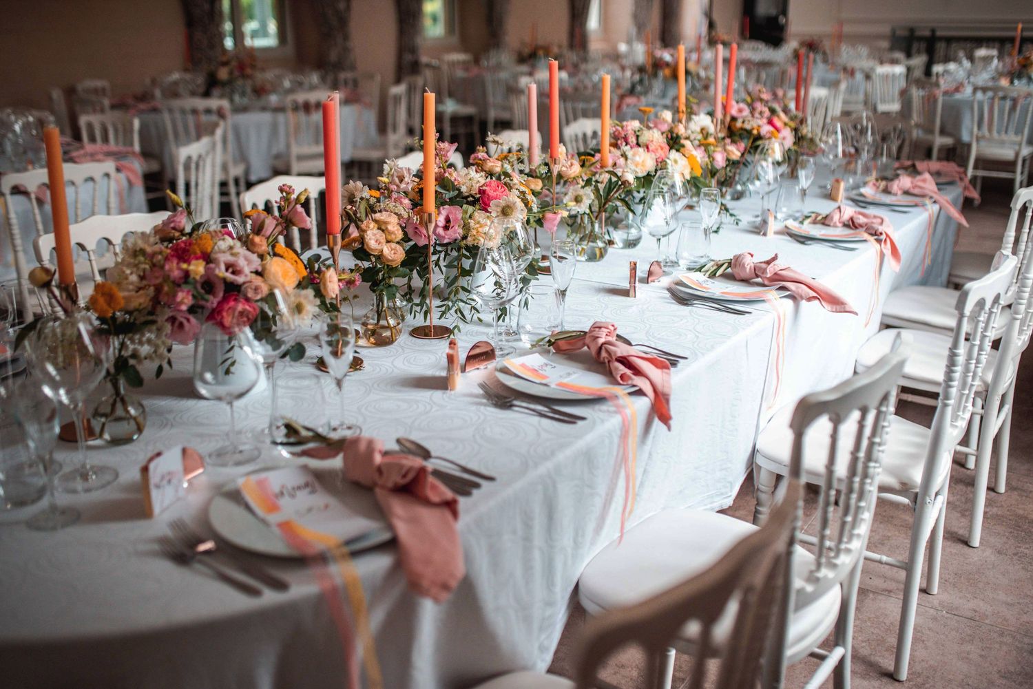 Elegant wedding reception tables set with coral accents and white chairs.