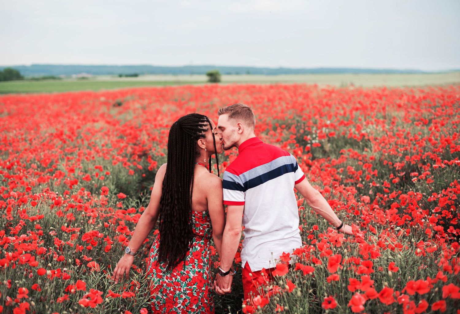 Couple walking through vibrant red poppy field on a sunny day.