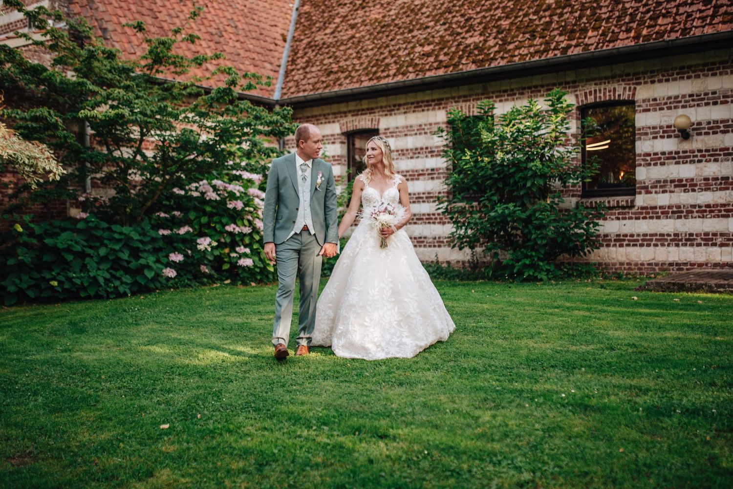 Wedding couple walking on grass with historic brick building in background.