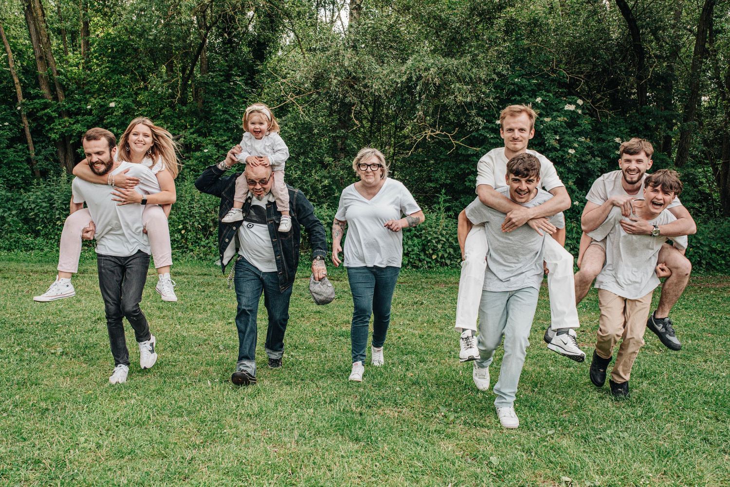 Joyful family running and playing together on green grass in coordinated white outfits.