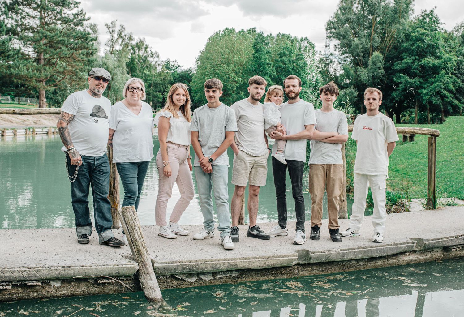 Family group standing together on a wooden dock by a lake surrounded by trees.
