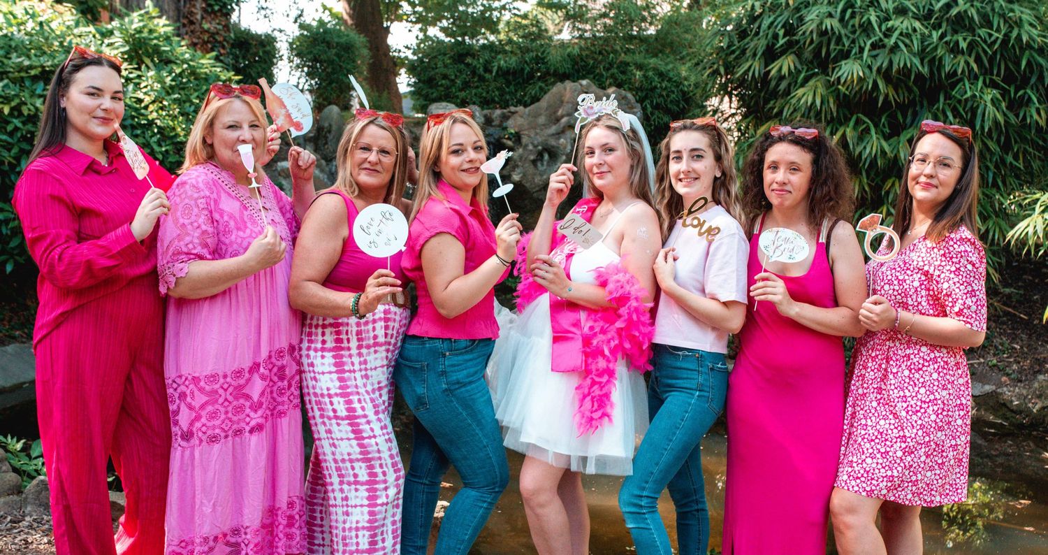 Friends in pink and colorful outfits pose together for a fun group photo in a garden setting.