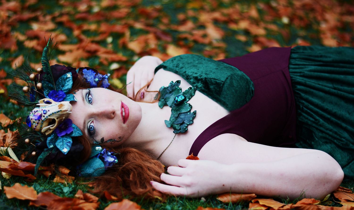 Romantic autumn photography with emerald dress and scattered leaves.