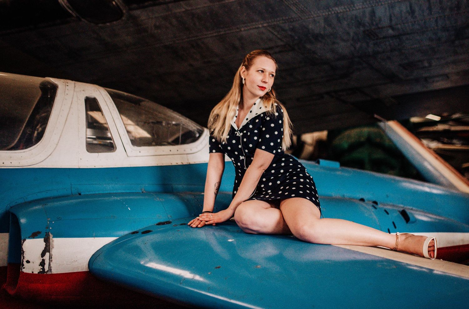 Woman in polka dot dress posing with vintage blue and white aircraft.