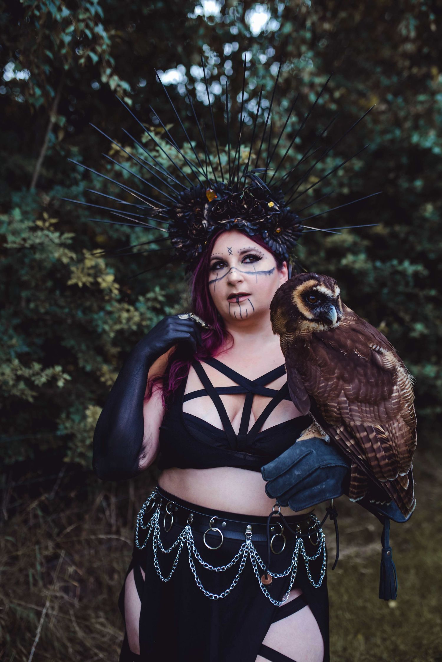 Gothic fantasy portrait featuring dark makeup, chains, and an owl in natural setting.