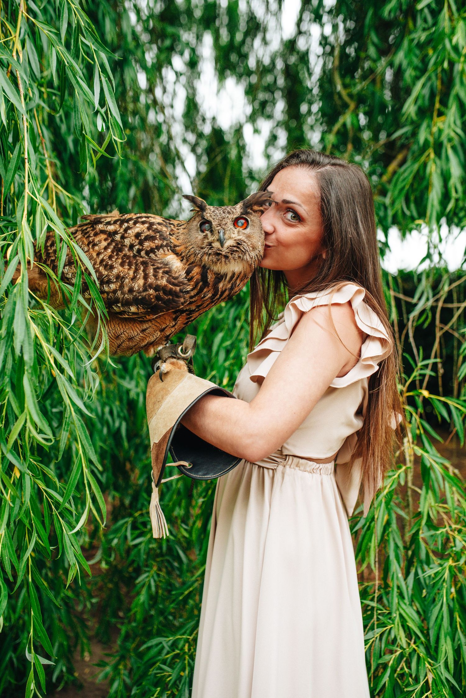 A white-dressed figure interacts with a Bengal cat against a backdrop of hanging willow branches.