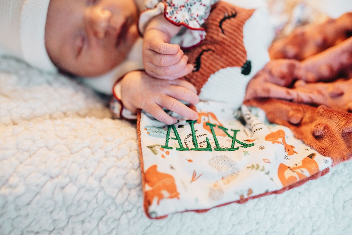 Newborn baby details with tiny hands and personalized blanket.