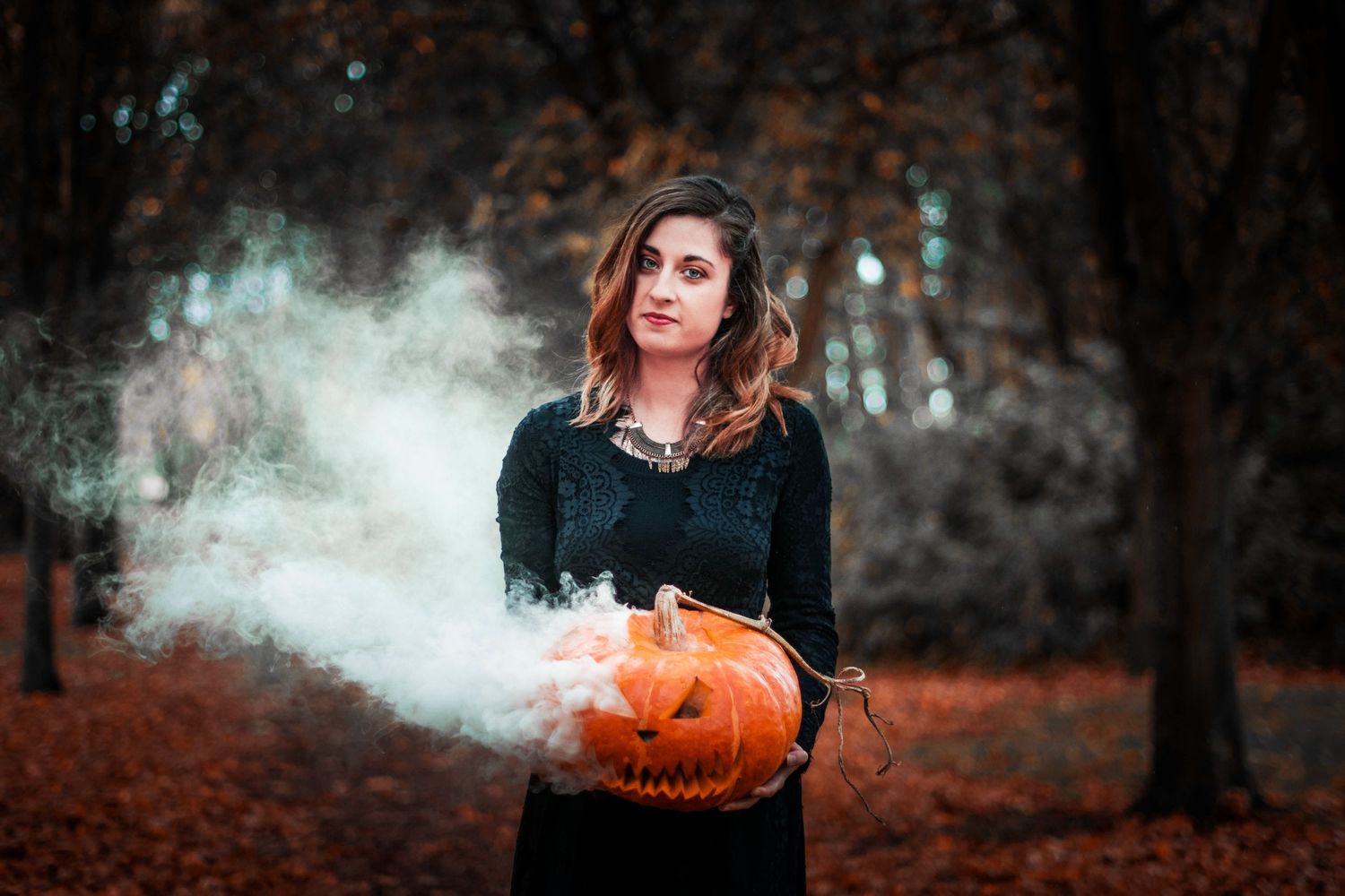 Moody autumn scene with carved pumpkin emitting smoke in dark forest setting.