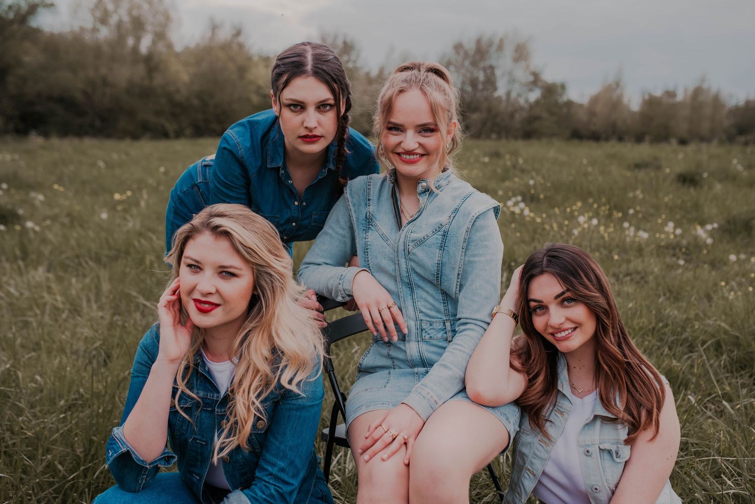 Group of friends in denim sitting together in a sunny meadow.