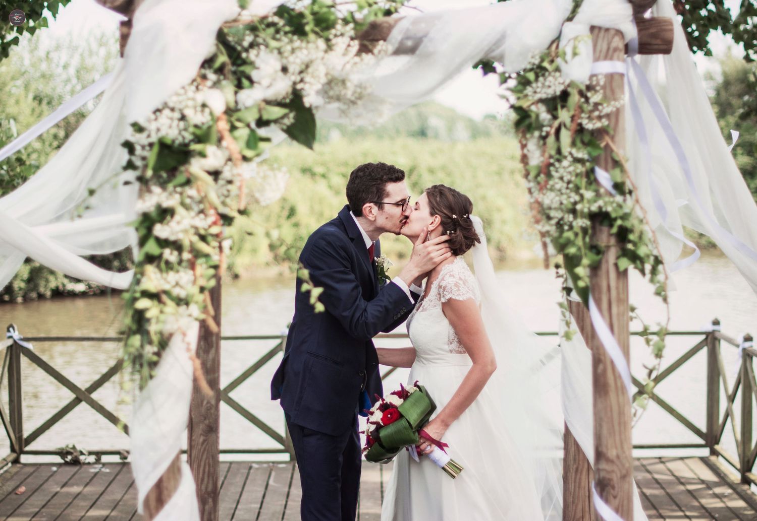 Wedding ceremony setup with white drapes and floral decorations on a wooden deck.