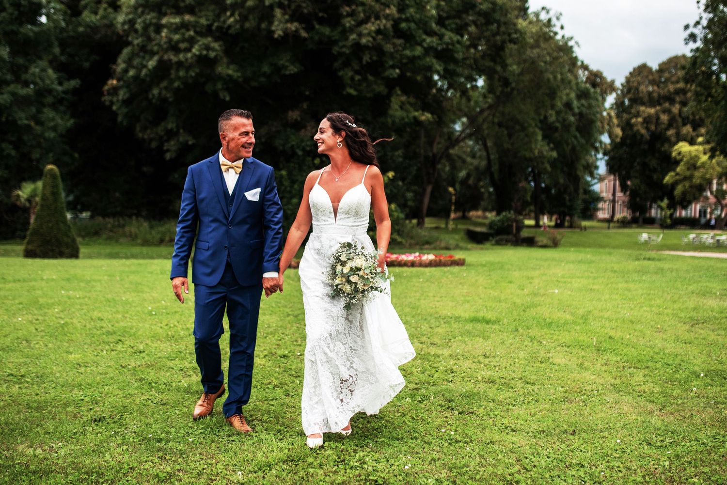 Couple walks hand in hand through a scenic green field on their wedding day.