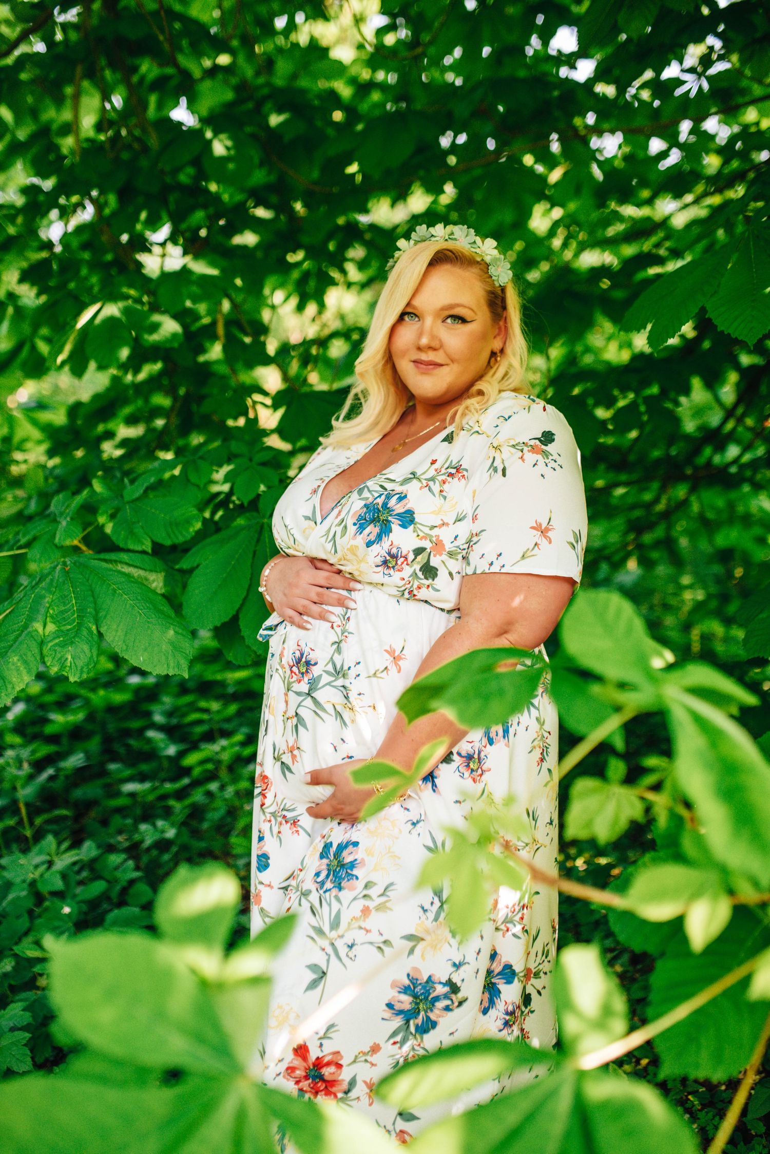 Maternity portraits taken in a lush green garden setting with natural sunlight filtering through leaves.