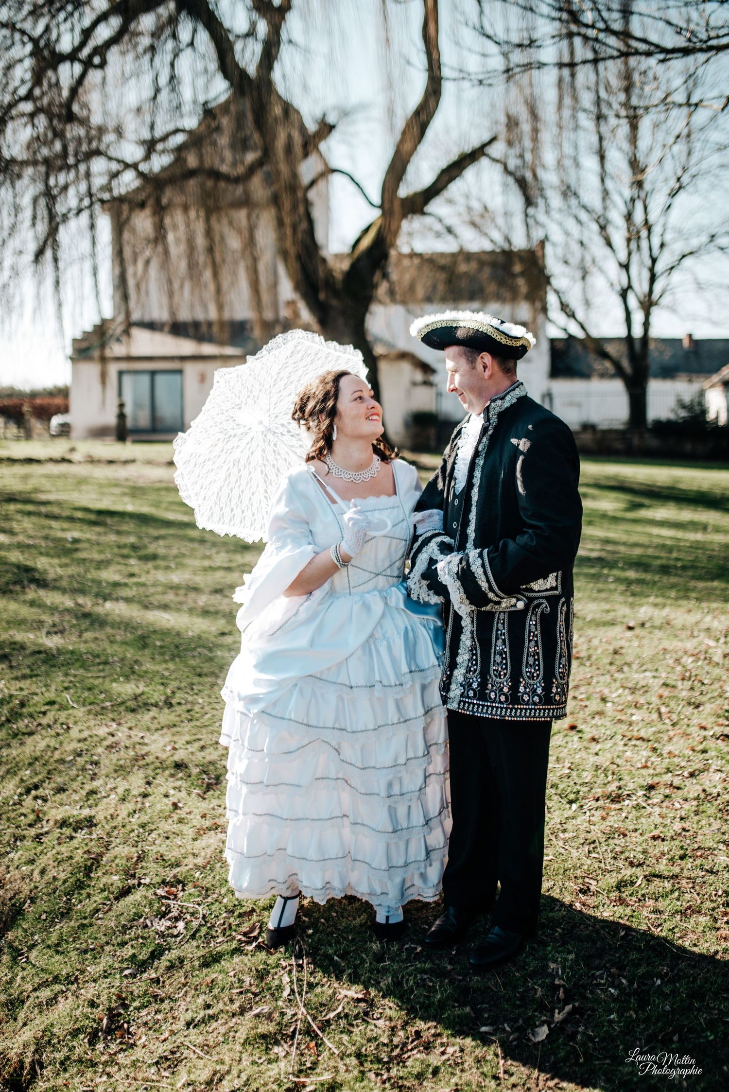 Couple in Victorian-era costumes posing outdoors on a sunny winter day.