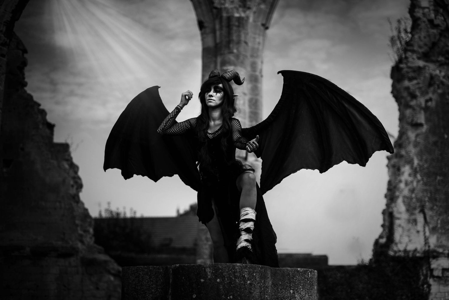 Gothic silhouettes with bat wings against dramatic sky in black and white composition.