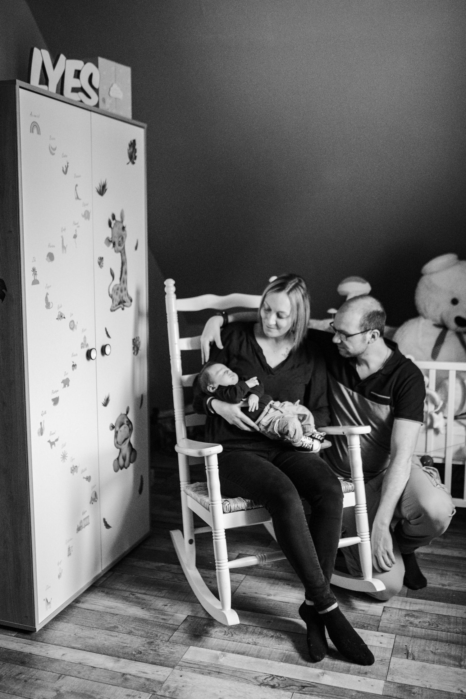 Black and white photo of a nursery scene with rocking chair and decorated wardrobe.