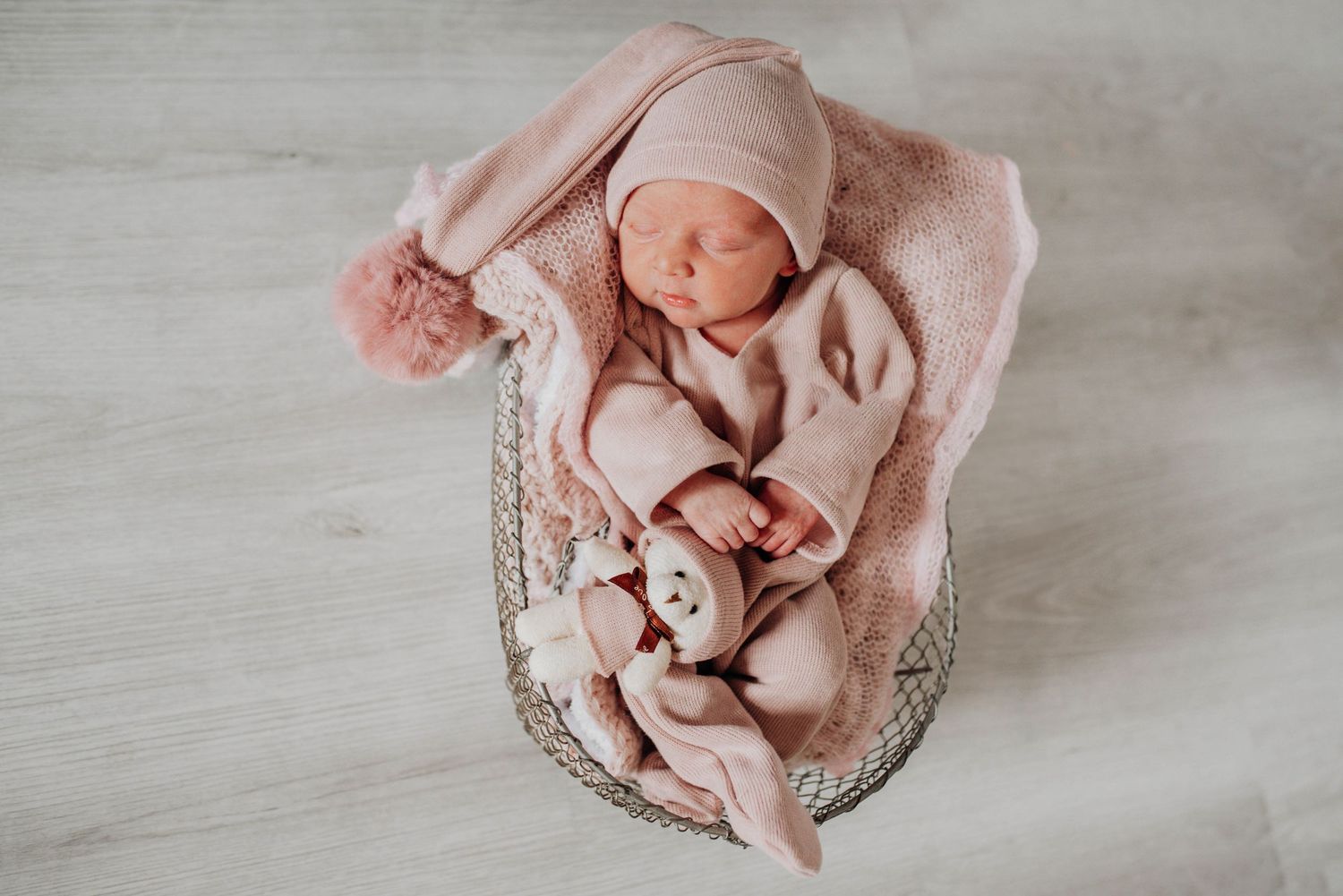 Sleeping newborn in pink outfit nestled in vintage-style basket with matching accessories.