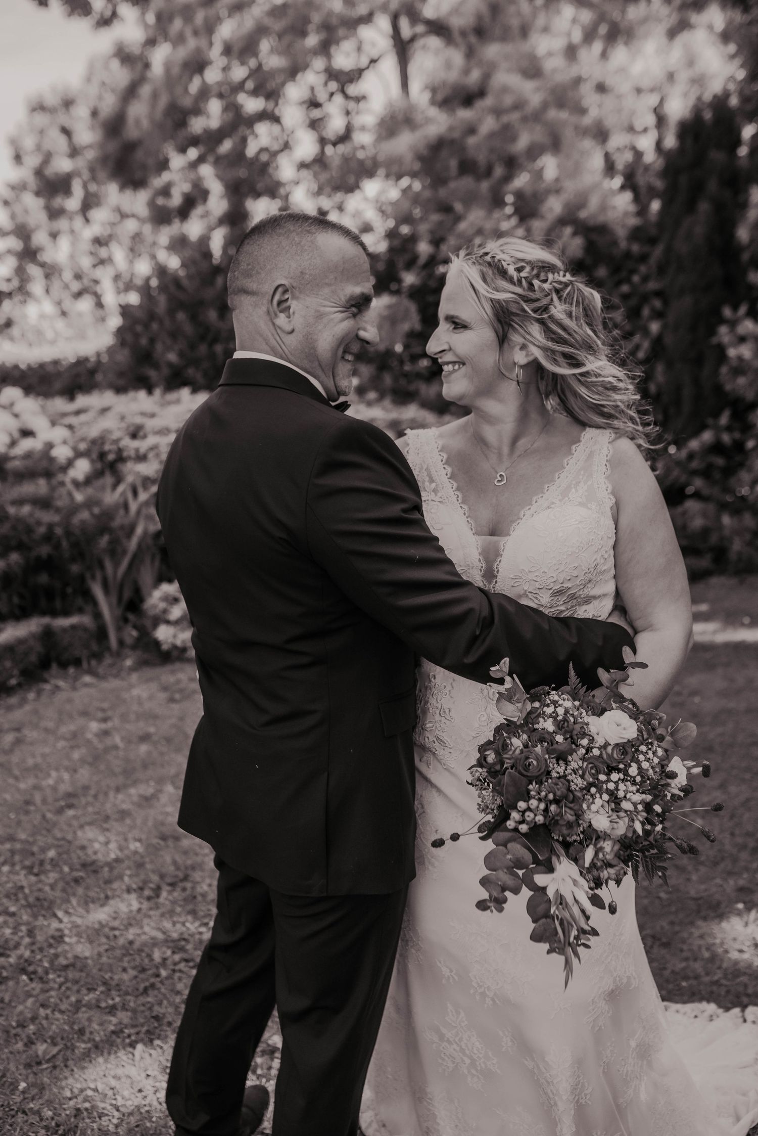 A black and white portrait captures a joyful moment between newlyweds with a floral bouquet.