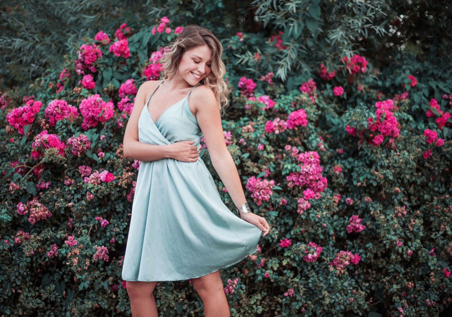 Fashion photography featuring mint dress against vibrant pink flowering bushes.