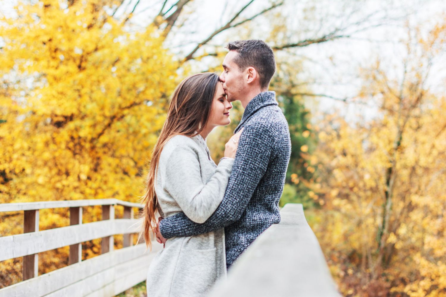 Couple embracing on wooden bridge surrounded by autumn foliage.