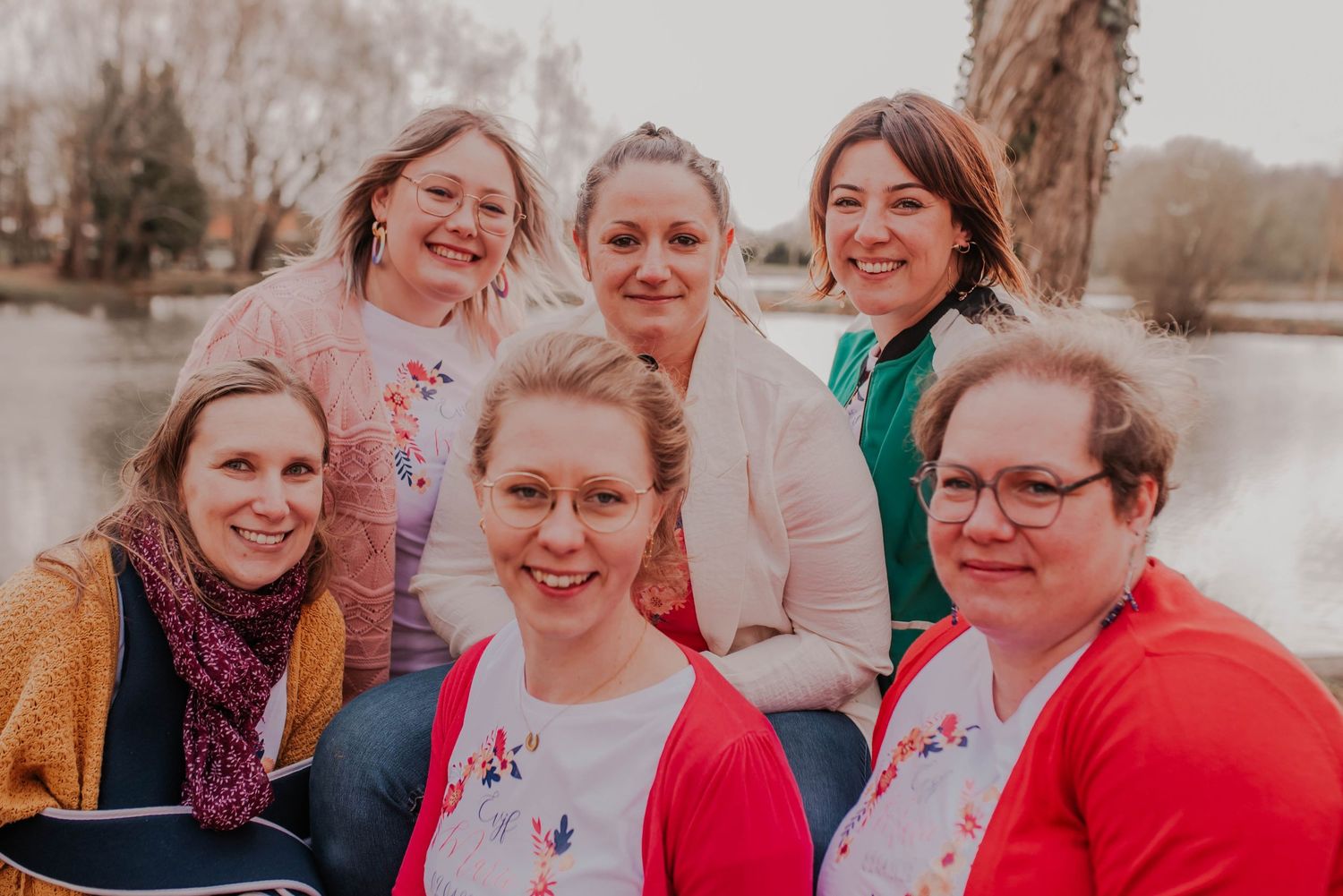 A group of friends smiling together outdoors on a cloudy day wearing colorful scarves and sweaters.