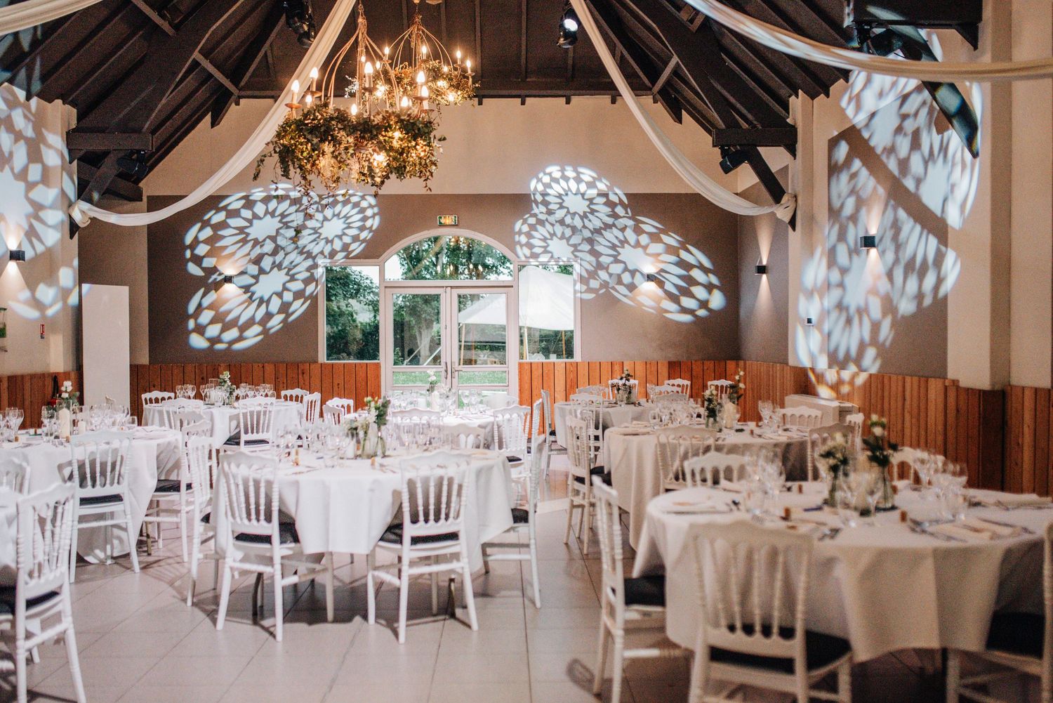 Grand wedding reception hall with white decor, chandeliers and draped fabric ceiling.