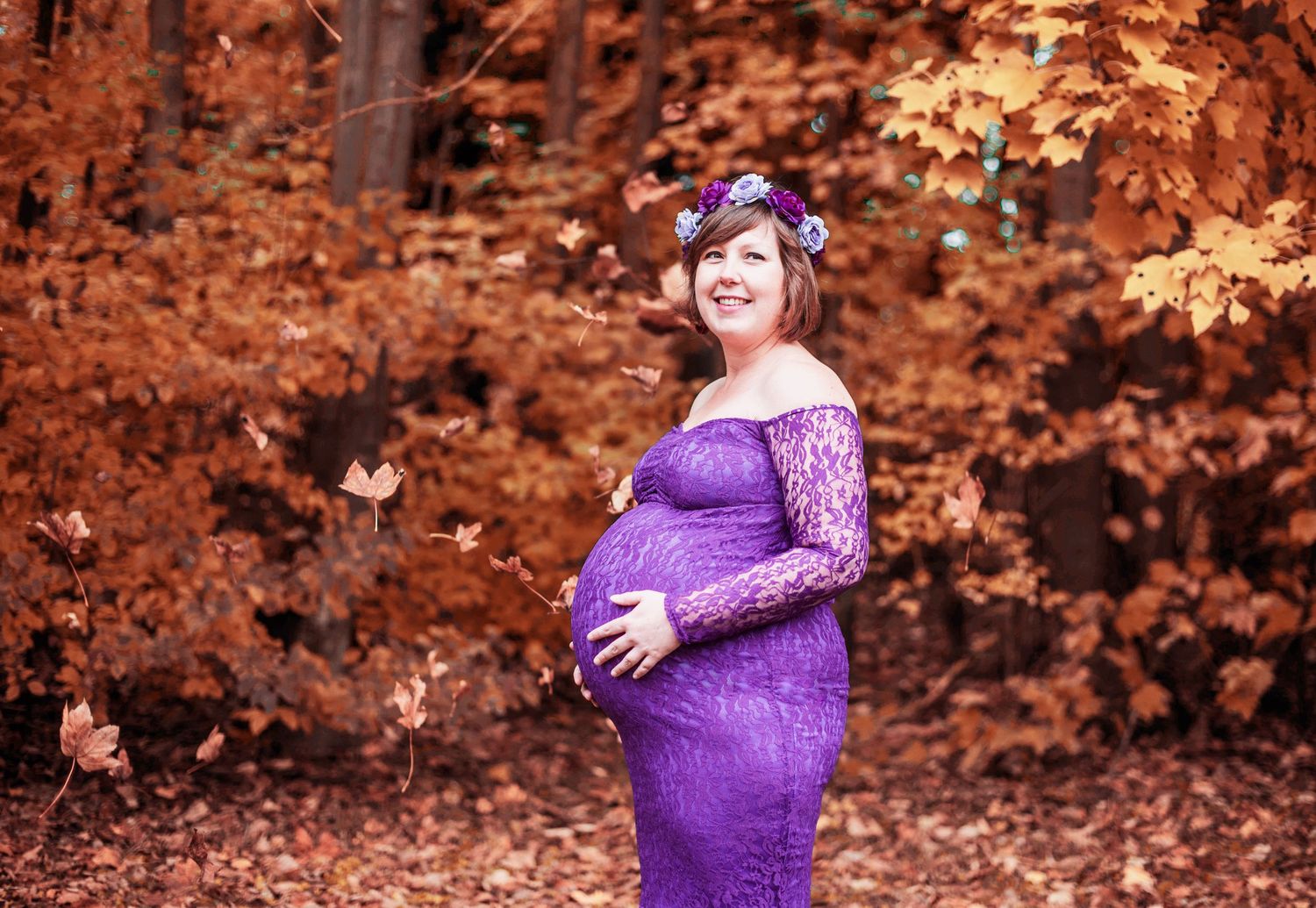 Maternity photos in purple dress against autumn foliage with warm orange tones.