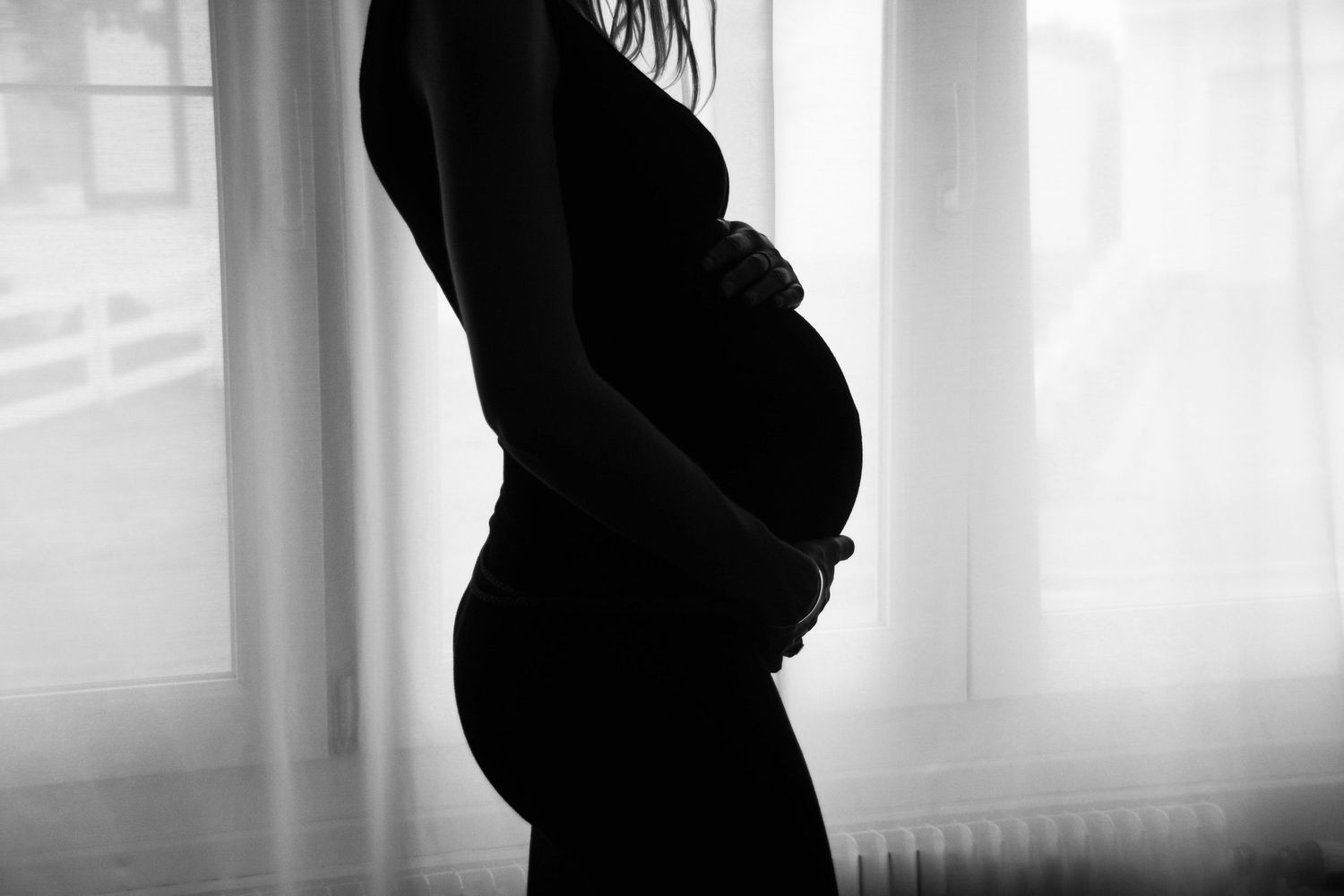 Black and white silhouette photos showing progression of pregnancy against window light.