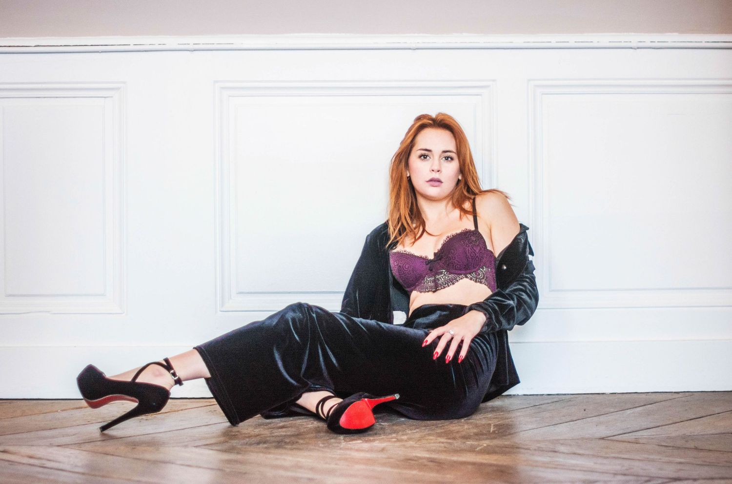 Artistic portrait session on wooden floor with minimalist white wall background.