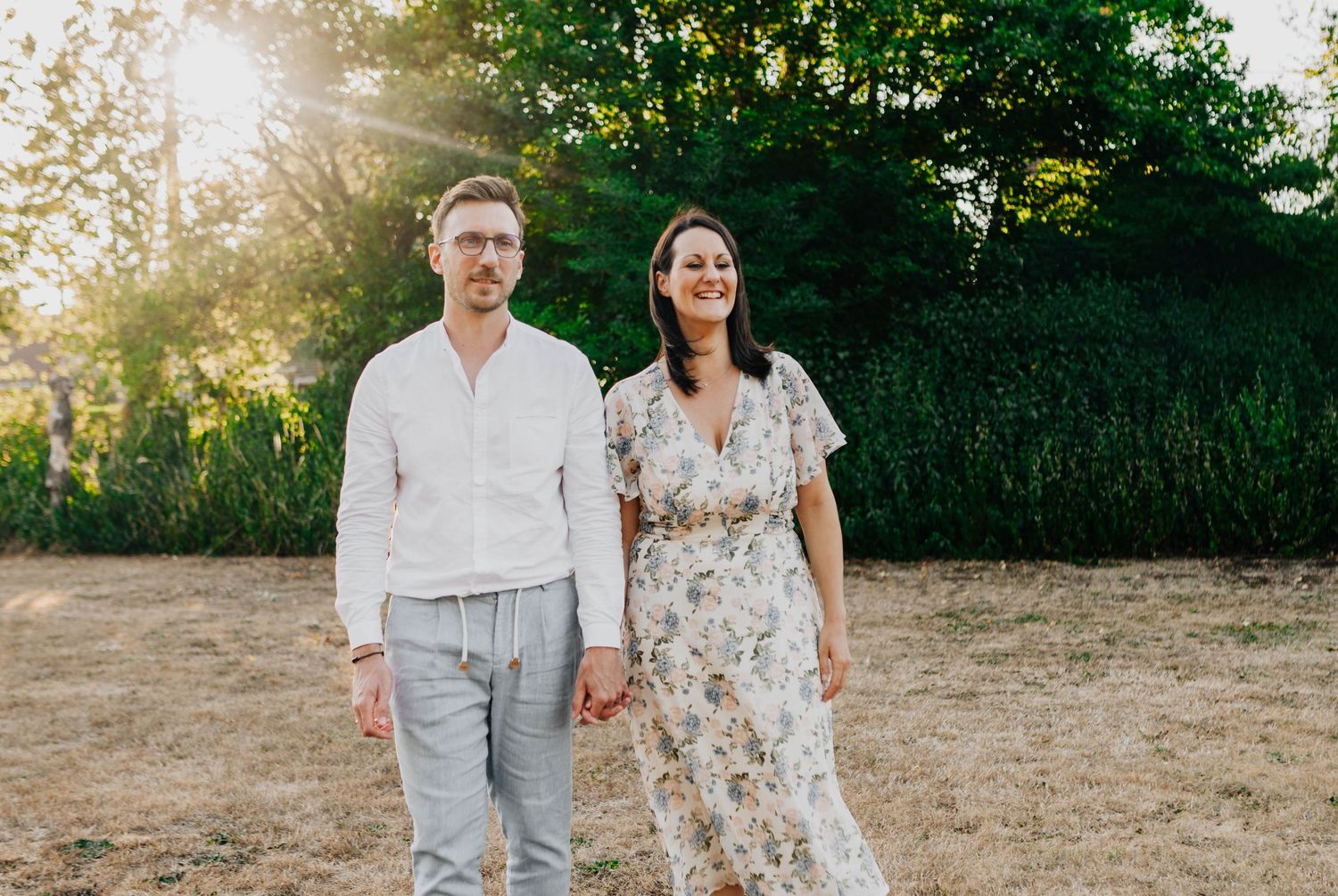 Couple in light summer attire holding hands at sunset in natural setting.