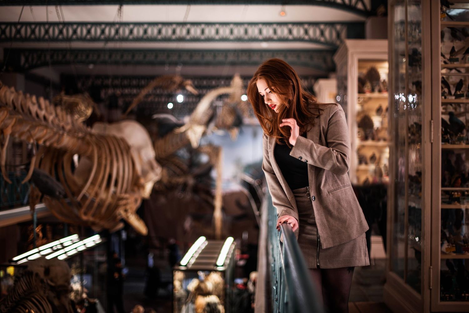 A moody indoor portrait in a museum with dinosaur skeletons in the background.