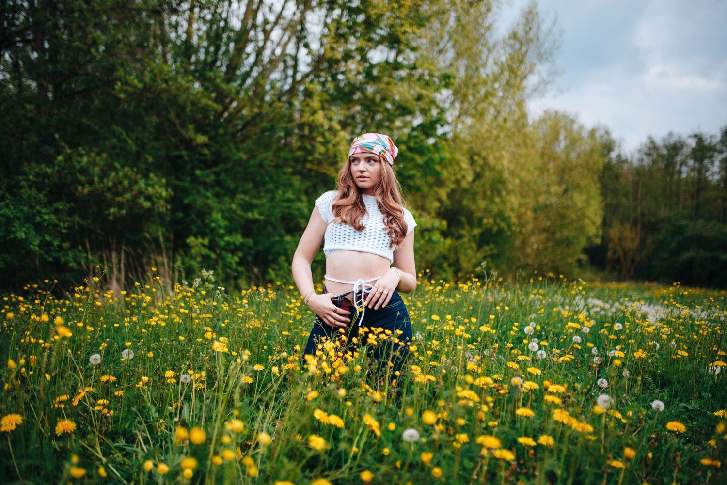 Woman in white top poses in field of yellow wildflowers during spring.