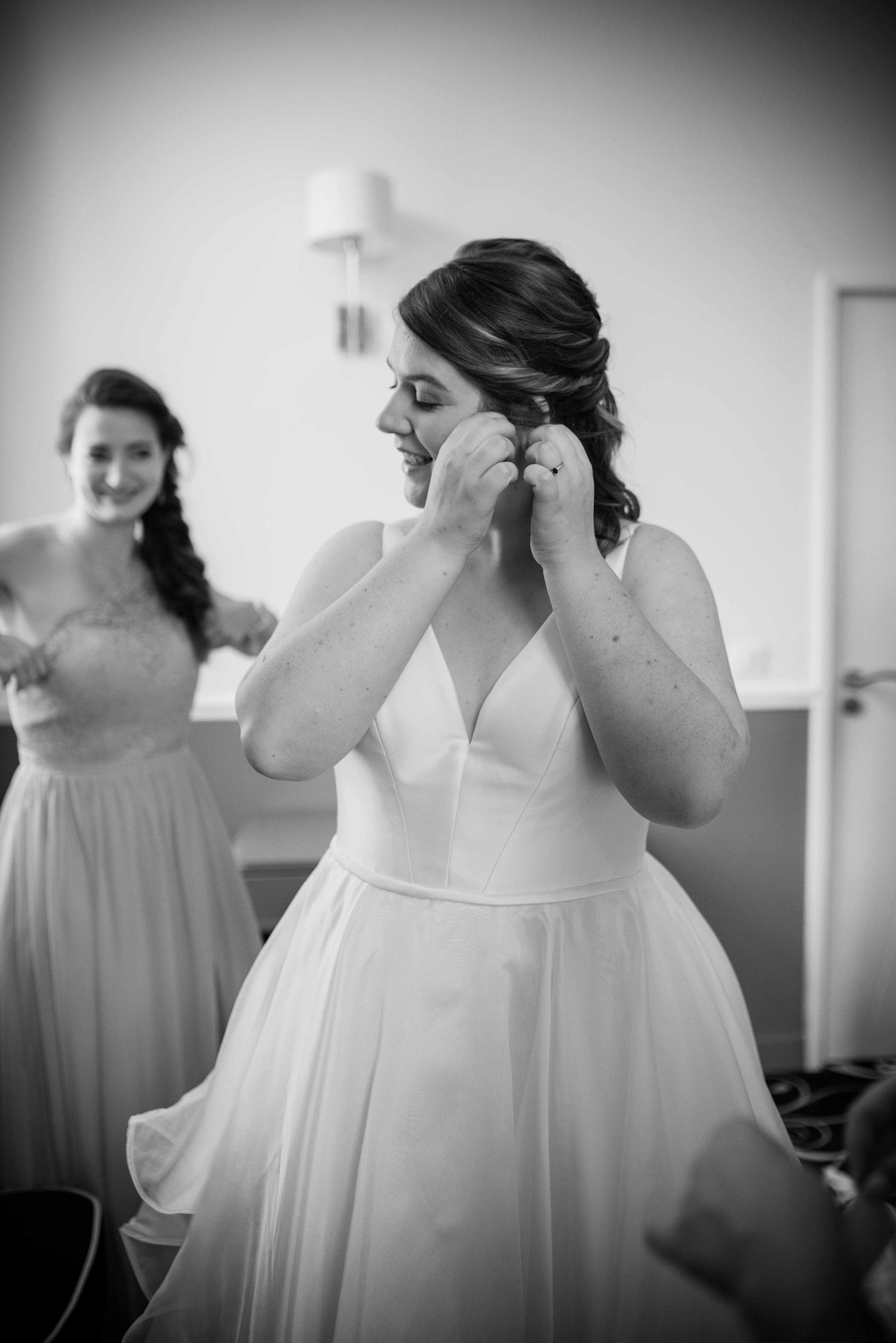 A tender moment during wedding preparations as a bride puts on her earrings in an elegant white gown.