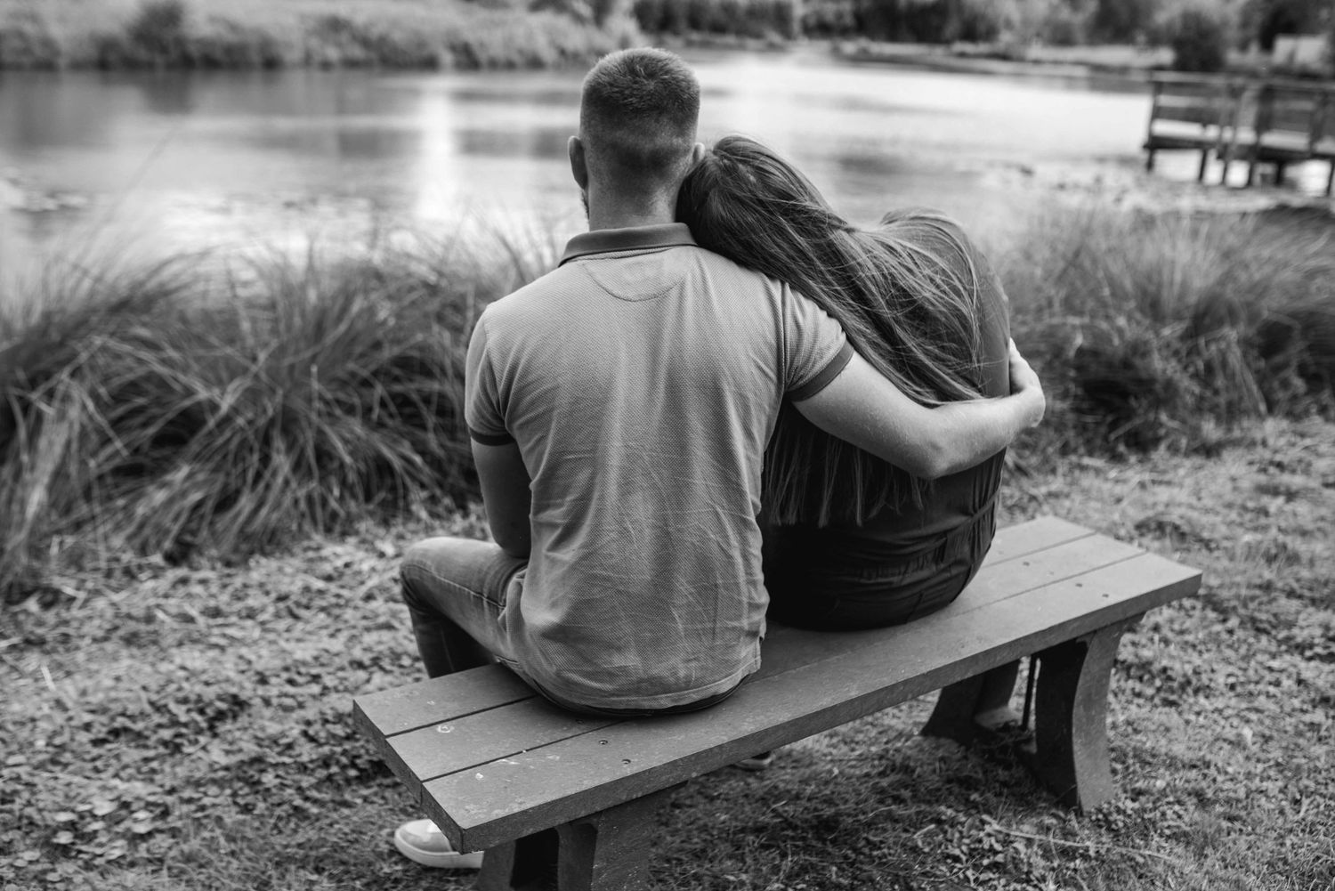 A couple relaxes on a wooden bench by a lake during a photo session.