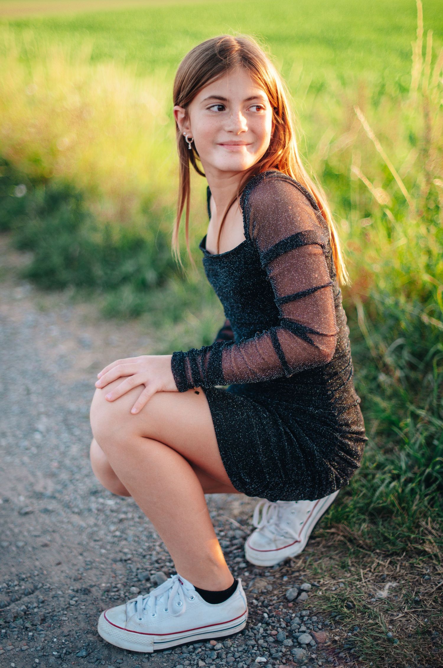 Young person in black sweater sitting on gravel path during golden hour photography session.