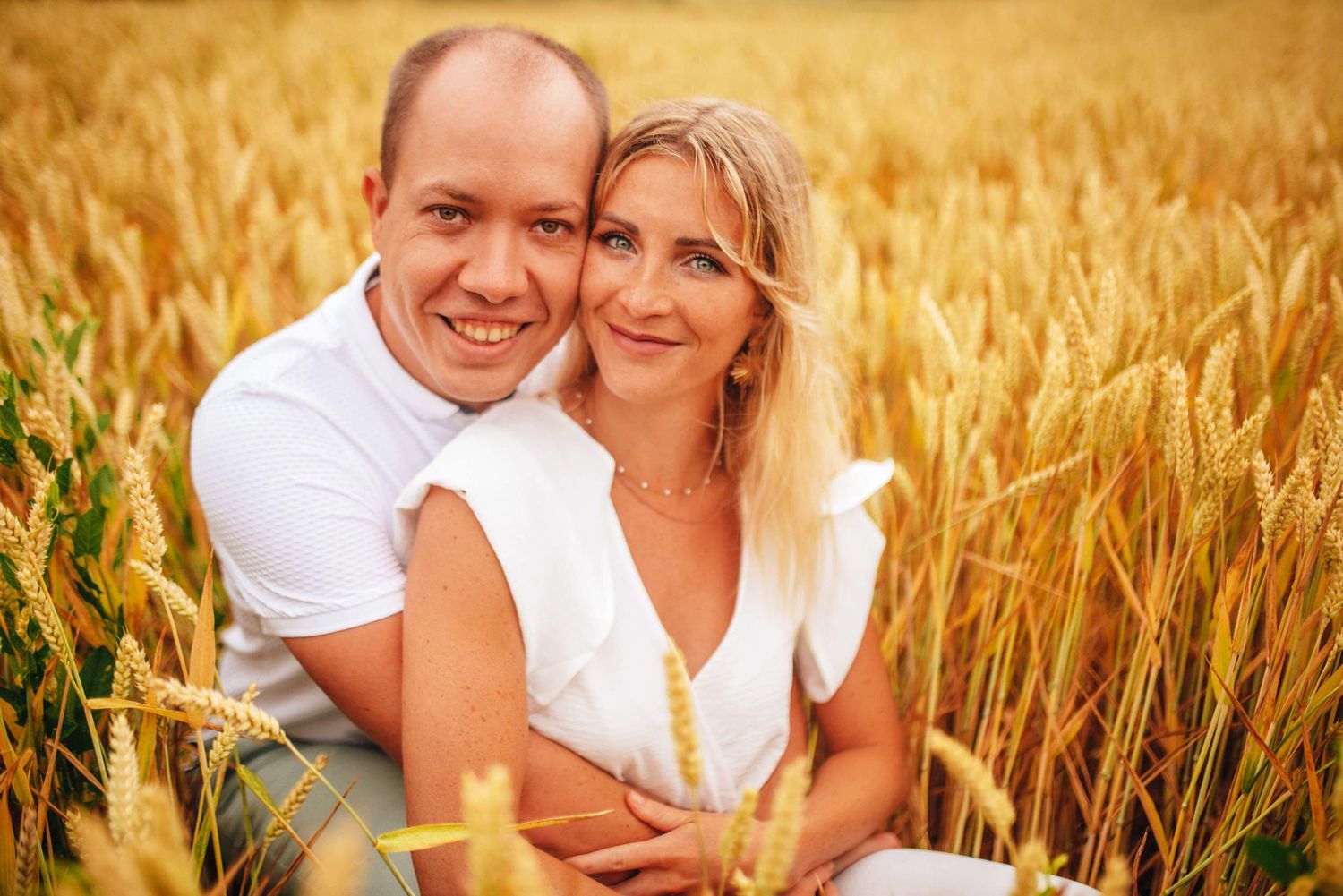 Loving couple embracing in golden wheat field at sunset.