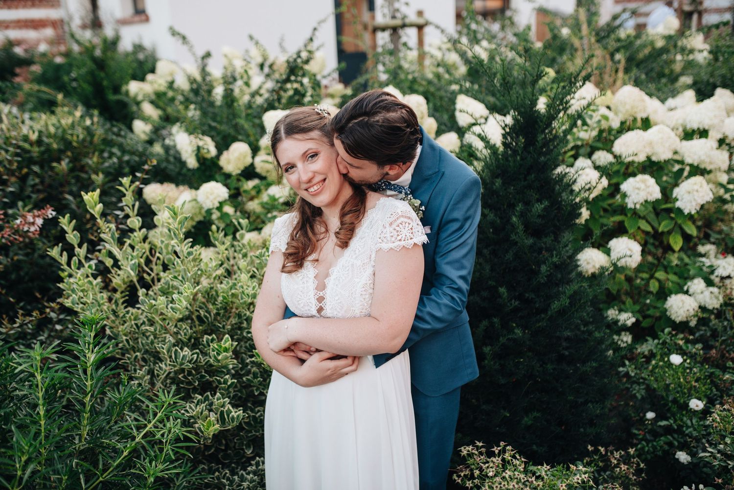 Romantic garden portraits among white roses and green shrubbery on wedding day.